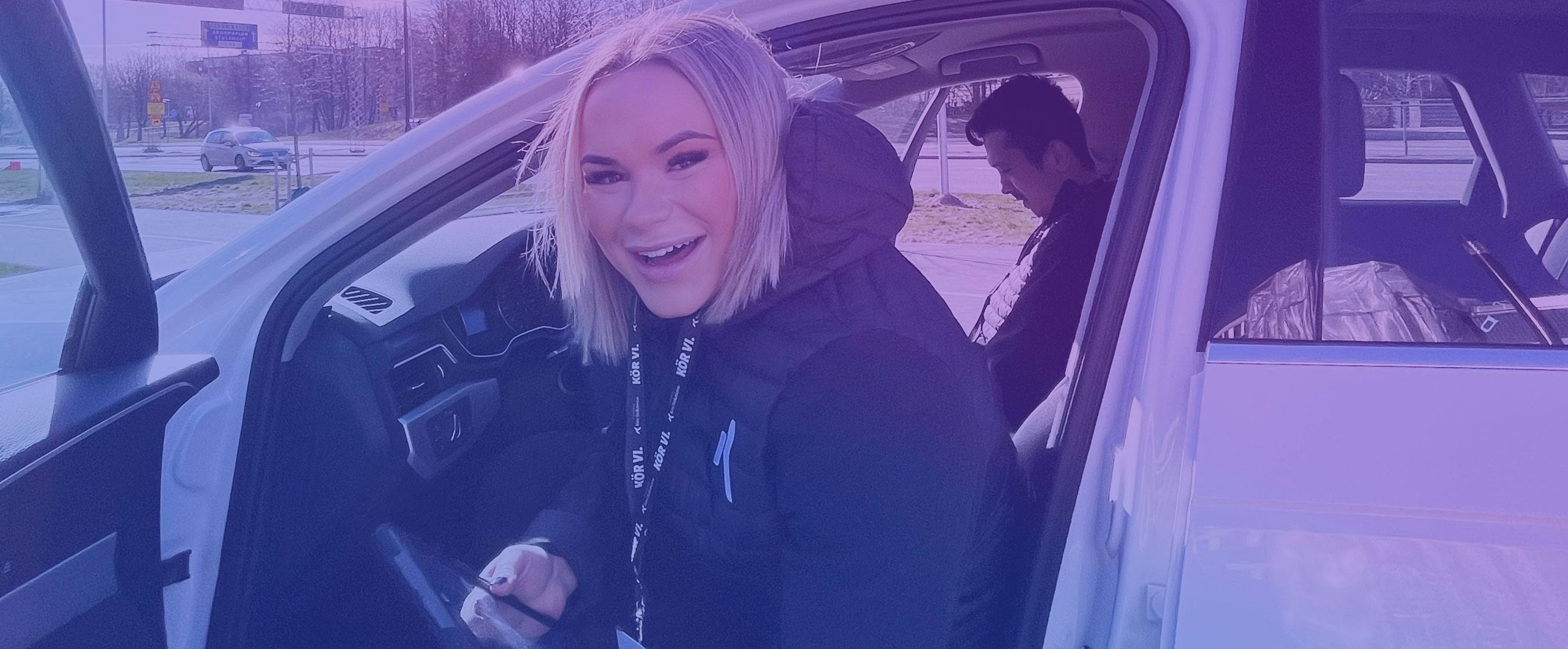 En kvinnlig fältsäljare sitter i sin tjänstebil och ler in i kameran.